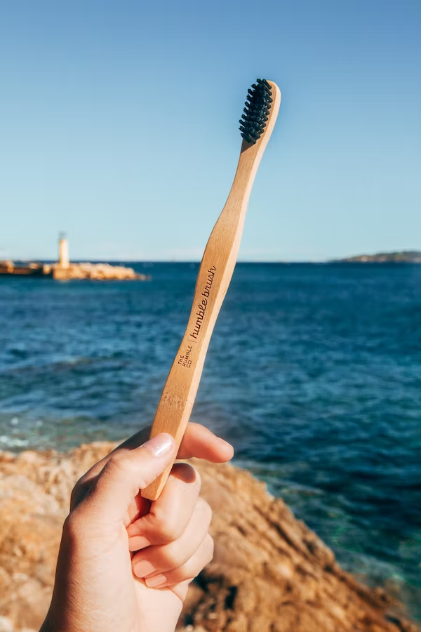 a hand holding a bamboo toothbrush nearby a body of water